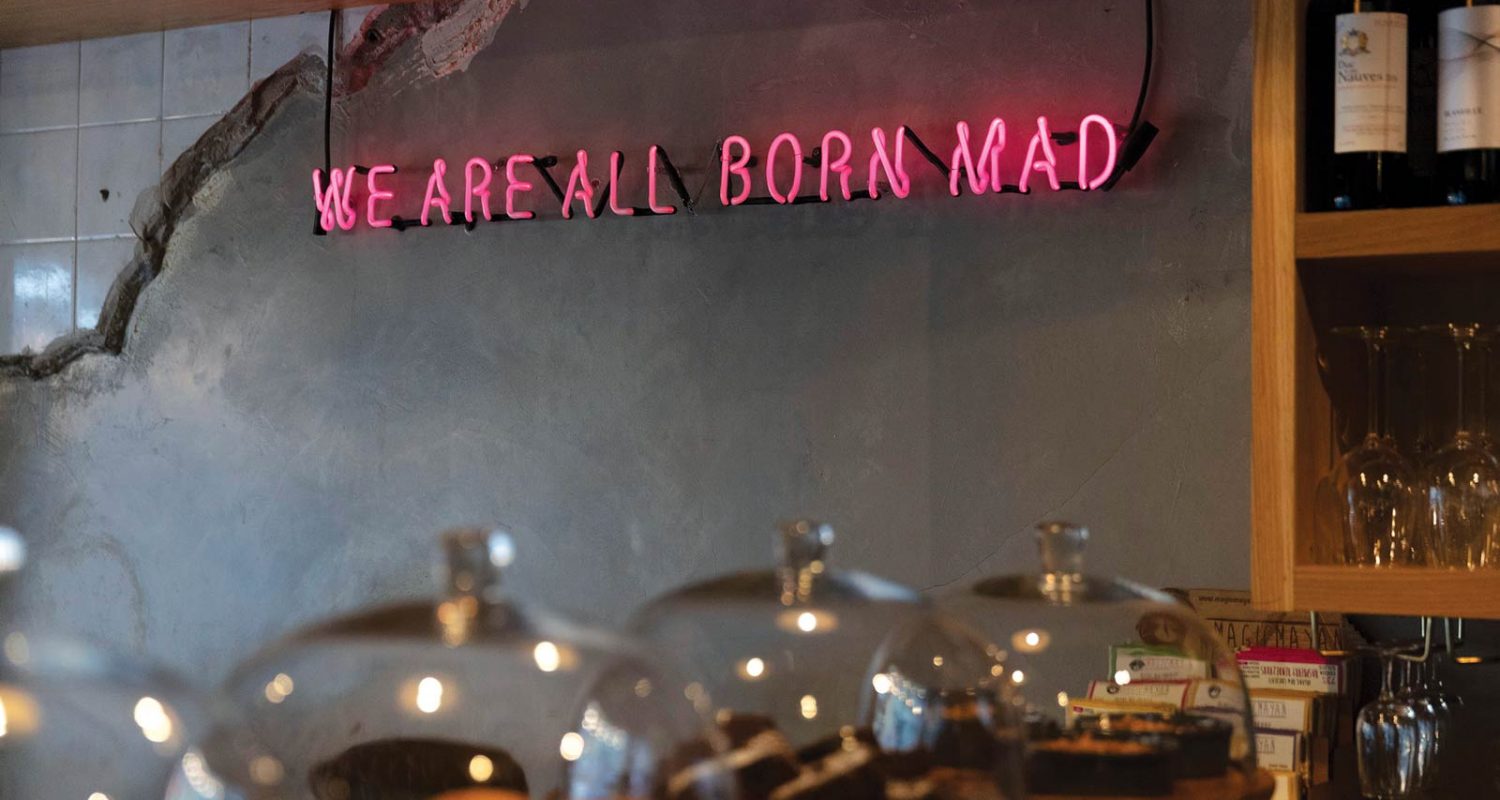Photograph of Crown Square bar, with neon sign reading "we are all born mad"