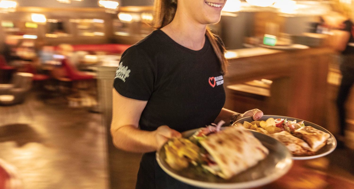 Smiling waitress at at Crown Square holding two plates food