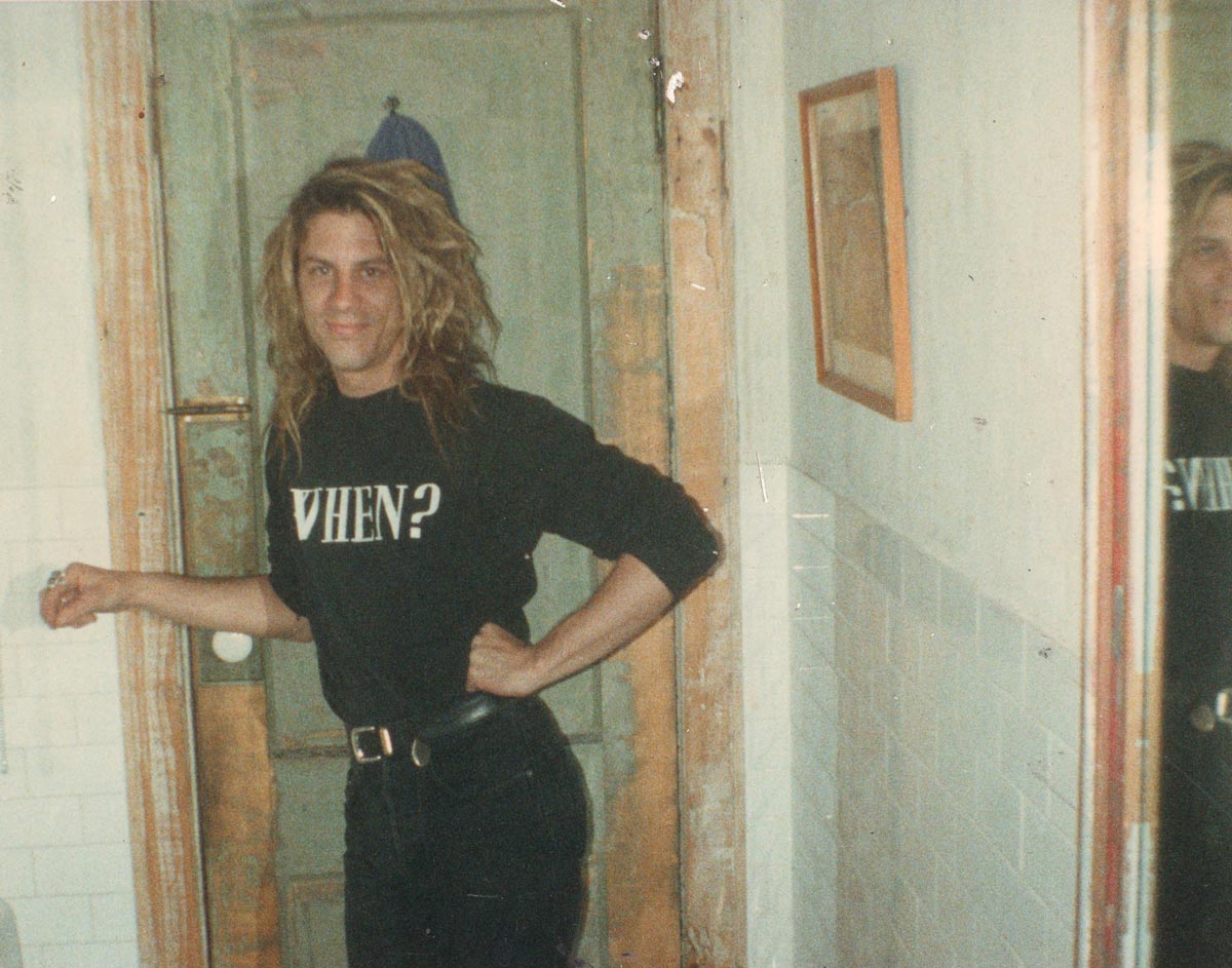 Old photo of person in hallway wearing black shirt that says "When?"