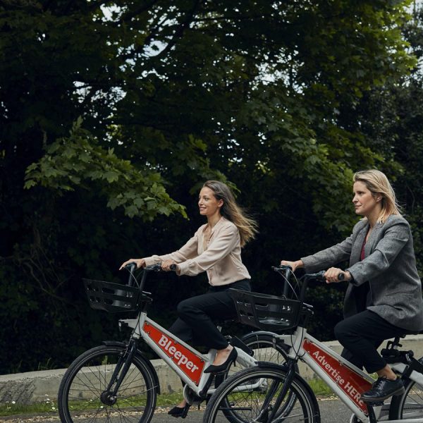Two women riding Bleeper bikes outside of Seamark after rebranding